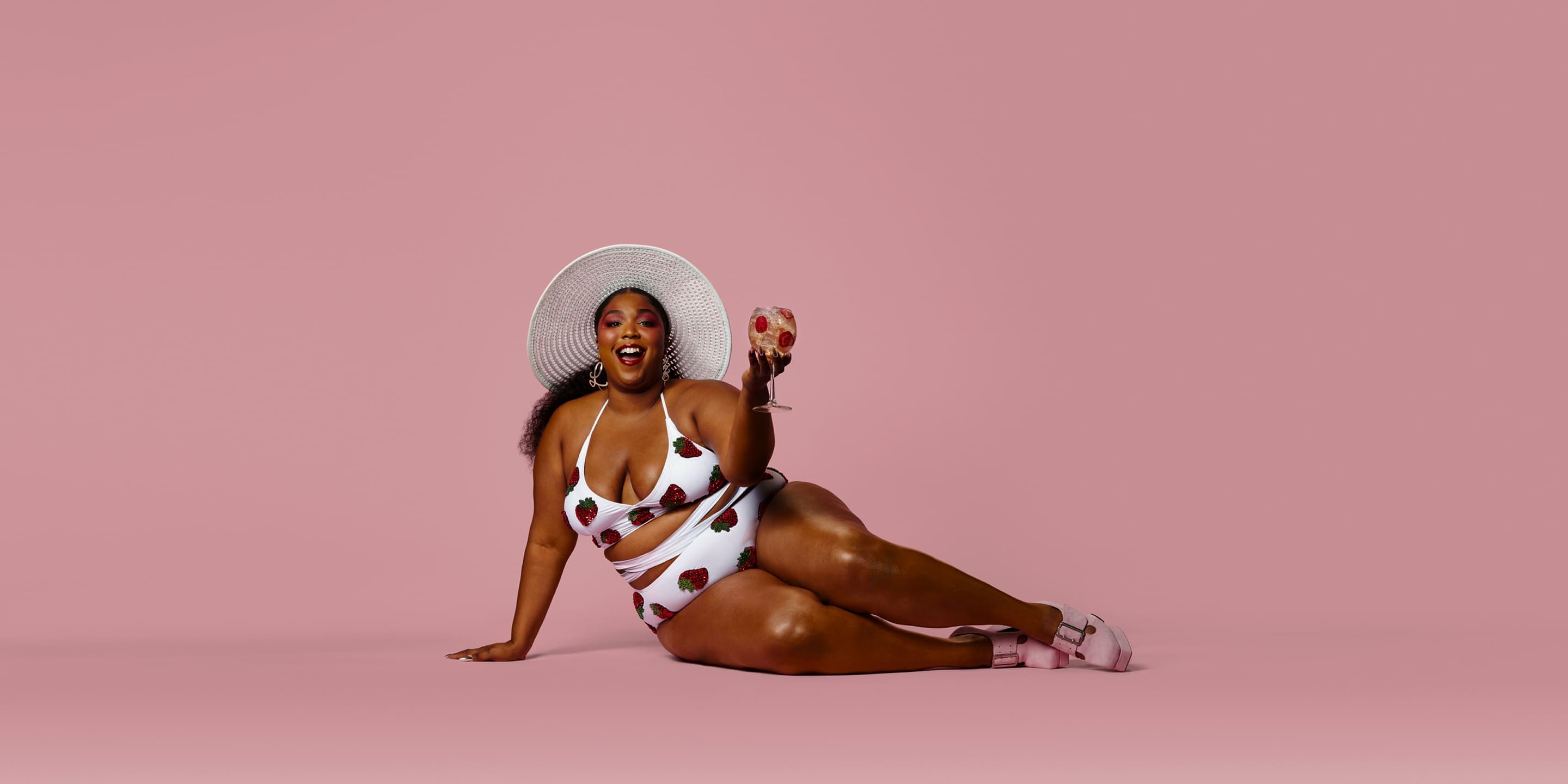 Left: Absolut Juice campaign portrait — model in a strawberry-print swimsuit and sun hat raising a glass against a pink backdrop. (1 of 2)